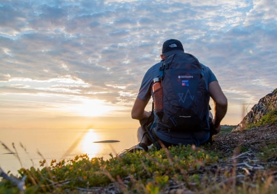 Man with FotoWare backpack looking at the sunset on a mountain by the sea